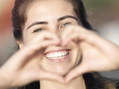Lächelnde Frau mit schönen Zähnen zeigt Herz