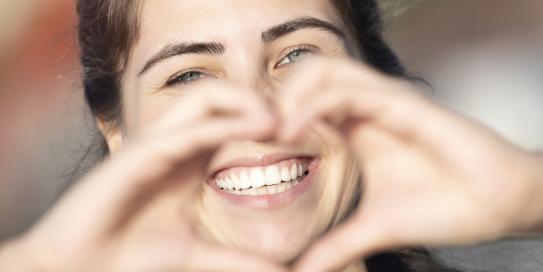 Lächelnde Frau mit schönen Zähnen zeigt Herz